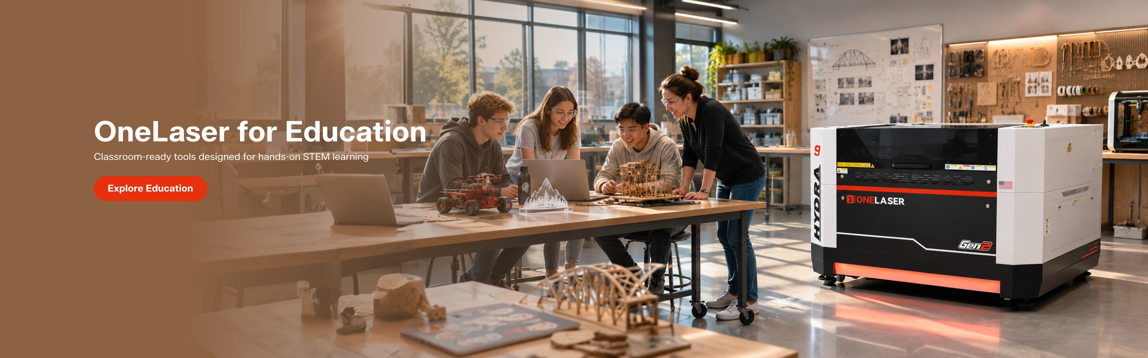 OneLaser for Education desktop laser cutter shown in a bright classroom or workshop setting, with several people gathered around a table working on laptops and assembling small objects. The product itself is visible on the right as a white, black, and orange laser cutter.